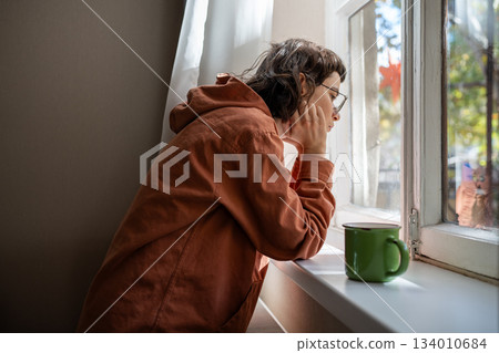 Introverted teen girl standing near window, looking at street indifferently, thinking of life 134010684