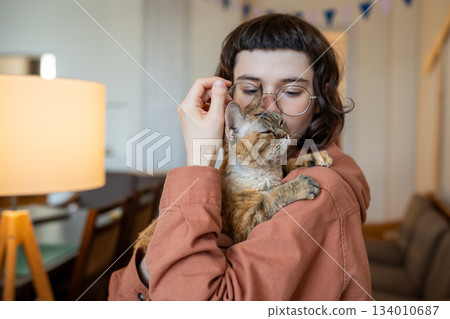 Cat owner caring woman hug kissing holding in hands loving pet at home. Therapy by domestic animal Cat owner caring woman hug kissing holding in hands loving pet at home. Therapy by domestic animal 134010687