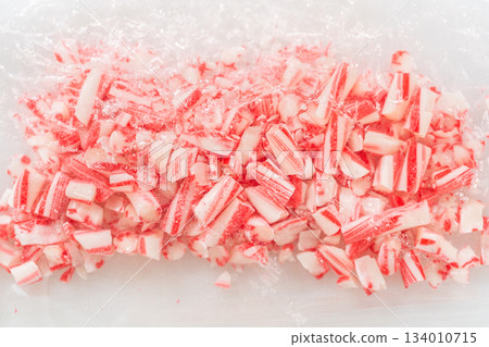 A close-up view of crushed candy canes scattered on a plastic bag, showcasing finely chopped red and white pieces for baking preparation. The perspective emphasizes texture and detail. A close-up view of crushed candy canes scattered on a plastic bag, showcasing finely chopped red and white pieces for baking preparation. The perspective emphasizes texture and detail. 134010715