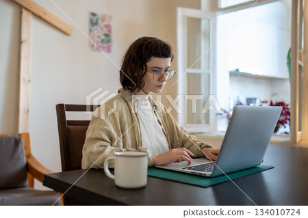 Concentrated teenager working, studying with laptop computer in comfortable conditions at home  134010724