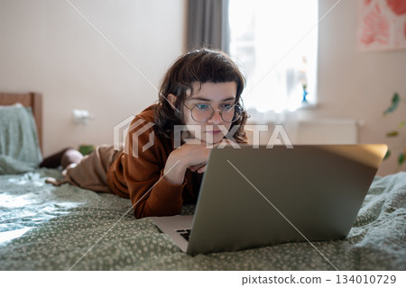 Interested teen girl spending weekend, pastime at home, watching video, film on laptop computer 134010729