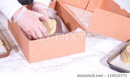 The sugar cookies, filled with sprinkles mixed into the dough, are carefully arranged with meticulous precision into a rustic brown paper box. 134010773