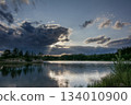 a view of a calm lake surrounded by forest under an impressive sky with clouds reflected in the water 134010900