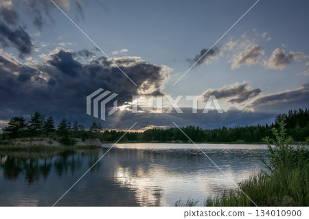 a view of a calm lake surrounded by forest under an impressive sky with clouds reflected in the water a view of a calm lake surrounded by forest under an impressive sky with clouds reflected in the water 134010900