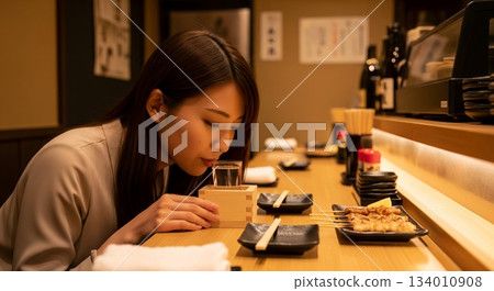 一位年輕女子將嘴直接貼在吧台上的酒杯上喝清酒。 134010908