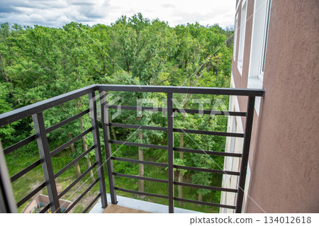 Modern balcony with metal railing overlooking green forest. 134012618