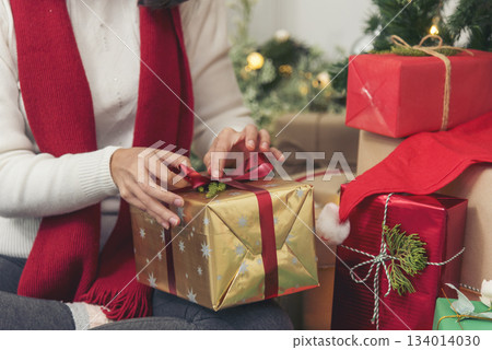 Close up woman hands wrap present gift in cozy living room. Woman wrapping christmas gift box under xmas tree. Asian woman decor bauble ball christmas tree in xmas holiday winter seasonal celebration 134014030