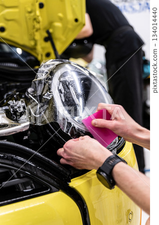 Paint protection film installation on car headlights using squeegee during professional PPF detailing Paint protection film installation on car headlights using squeegee during professional PPF detailing 134014440