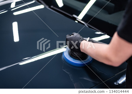 Machine polishing and paint correction on glossy black car hood during professional car detailing 134014444