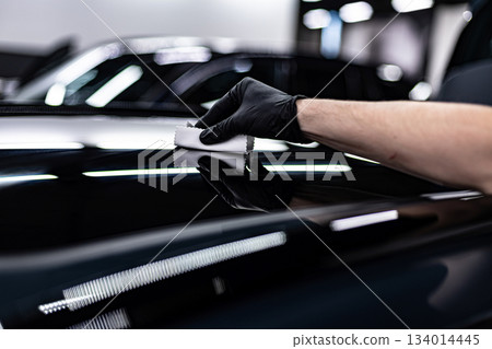 Ceramic coating application during professional car detailing on glossy black vehicle in modern detailing studio 134014445