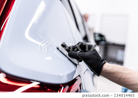 Ceramic coating application on rear car body panel near taillight during professional car detailing 134014465