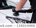 Machine polishing and paint correction on white car hood near headlight during professional car detailing 134014466