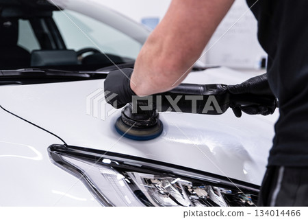 Machine polishing and paint correction on white car hood near headlight during professional car detailing 134014466