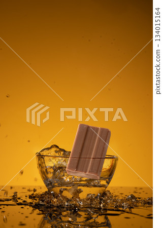 A soap bar falls into a bowl of water creating splashes and droplets. The bright color of the background adds to the scene. Water surrounds the soap as it lands. 134015164