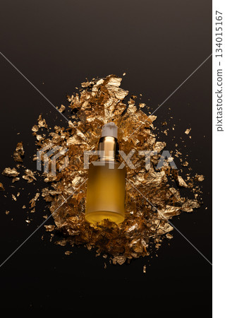 A beauty serum bottle is placed on a bed of gold leaf. The setting highlights the bottle and the shiny gold showing off the product in a studio space. 134015167