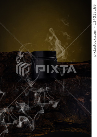 black cosmetic jar sits on a textured wooden surface. White smoke curls around the jar in a dimly lit setting. The atmosphere is focused on the jar and the smoke effect. black cosmetic jar sits on a textured wooden surface. White smoke curls around the jar in a dimly lit setting. The atmosphere is focused on the jar and the smoke effect. 134015169