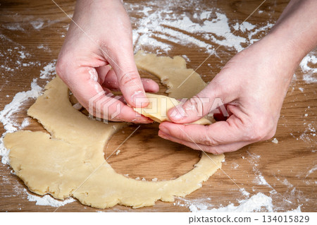 Hands Shaping Raw Dough Circle on Floured Wooden Surface During Pastry Preparation 134015829