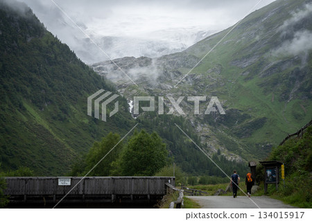 Hikers couple walking the alpine valley towards massive glacier ahead of them, Austrian Alps Hikers couple walking the alpine valley towards massive glacier ahead of them, Austrian Alps 134015917