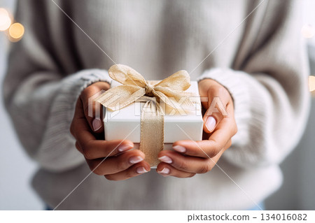 Gift wrapped with care held by person in cozy sweater during festive season Gift wrapped with care held by person in cozy sweater during festive season 134016082
