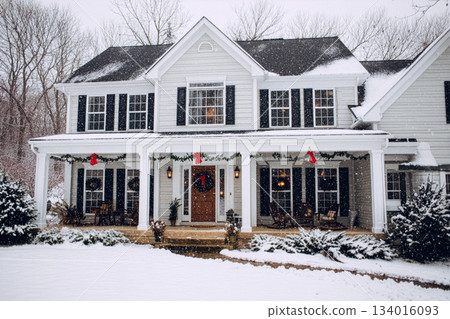Charming white house decorated for winter with snow-covered porch and festive wreath in a peaceful snowy neighborhood setting 134016093