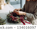 Crafting a beautiful holiday wreath with fresh greenery and decorative berries in a cozy space during winter season 134016097
