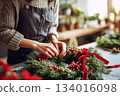 Creating a beautiful Christmas wreath with natural greens and red berries in a cozy workshop during the holiday season 134016098