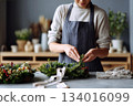 Creating beautiful holiday wreaths with fresh greenery in a cozy workshop during the festive season 134016099