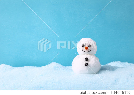 Cute snowman with a cheerful smile stands on soft snow against a bright blue background during winter 134016102