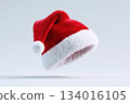 Bright red Christmas hat with white fluffy trim floating against a simple gray background, evoking holiday spirit and festive excitement during the winter season 134016105