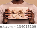 Hands hold a beautifully wrapped gift with a bow against a neutral background, perfect for celebrating special occasions 134016109