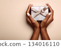 Elegant gift box held gently in hands against a minimalistic background showcasing simplicity and anticipation for celebration or special occasion 134016110