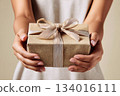 Present wrapped in brown paper held by hands with elegantly tied ribbon in a neutral-toned setting 134016111