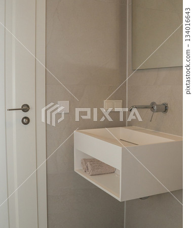 Minimalist bathroom interior with a floating white sink, neutral ceramic tiles, and clean contemporary lines. Soft lighting and functional design highlight modern home decor, renovation themes, and Minimalist bathroom interior with a floating white sink, neutral ceramic tiles, and clean contemporary lines. Soft lighting and functional design highlight modern home decor, renovation themes, and 134016643