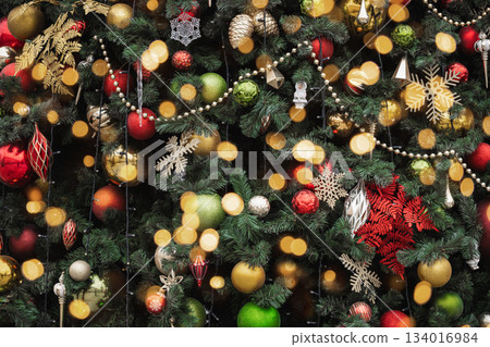 Festive decorated Christmas tree with colorful ornaments and glowing lights. Holiday background with warm bokeh effect. 134016984