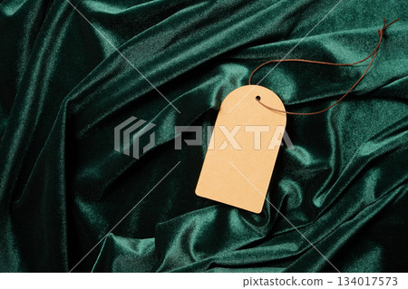 Blank brown tag resting on luxurious green velvet cloth with elegant drapes 134017573