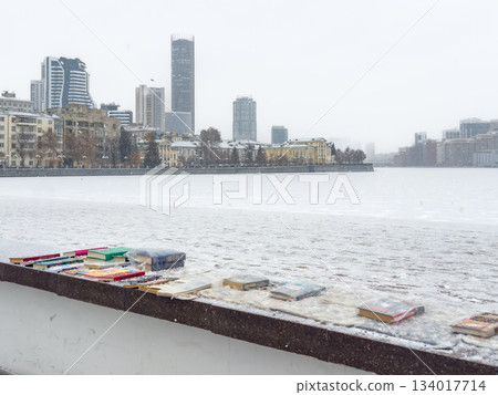 Bright vessels rest by icy river bank, Colorful boats lined up on snowcovered urban quay Bright vessels rest by icy river bank, Colorful boats lined up on snowcovered urban quay 134017714