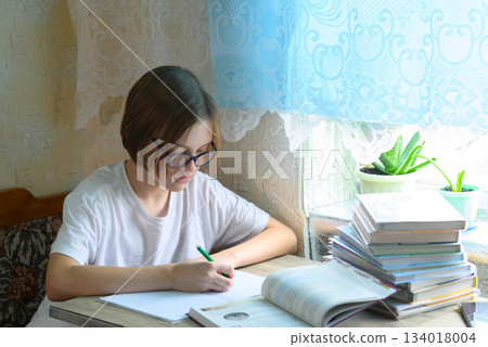 student in glasses writing with a pen in a notebook at home student in glasses writing with a pen in a notebook at home 134018004