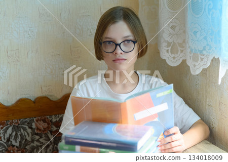 teen boy in glasses reading a textbook and looking at camera teen boy in glasses reading a textbook and looking at camera 134018009
