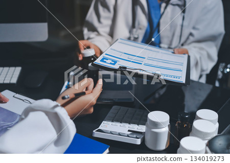 Two doctors and a female nurse meet at a table in the hospital, collaborating on medical tasks using laptops and computers 134019273