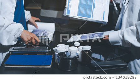 Two doctors and a female nurse meet at a table in the hospital, collaborating on medical tasks using laptops and computers 134019282