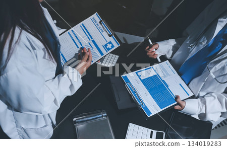 Two doctors and a female nurse meet at a table in the hospital, collaborating on medical tasks using laptops and computers 134019283