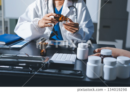 Female doctor holding a medicine bottle is checking the quality of medicine for any side effects the patient or not and recording patient information at the hospital. medical and health care concept 134019298