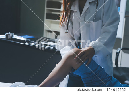 Doctor examining and supporting injured ankle of female patient in hospital room, providing medical assistance and treatment for sprain or fracture 134019332