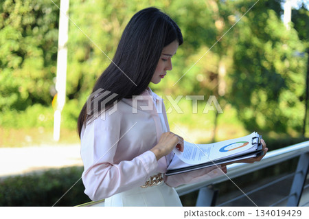 Female professional reviewing documents outdoors in a semi-urban office. Female professional reviewing documents outdoors in a semi-urban office. 134019429