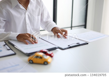 A man signing a contract for a car loan, lease, vehicle registration or insurance policy.Concept for Sales Contract, Financing Agreement, Insurance Policy, Vehicle Registration. A man signing a contract for a car loan, lease, vehicle registration or insurance policy.Concept for Sales Contract, Financing Agreement, Insurance Policy, Vehicle Registration. 134019705