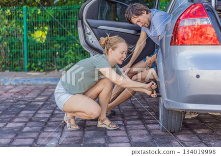 Woman changing a car wheel while a man watches, showing confidence and independence. Gender equality, empowerment and modern feminism concept, representing strength, self-reliance and breaking 134019998