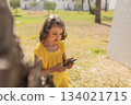 Girl 7 years old in yellow dress talking on video call on phone on lawn with palm trees in summer day 134021715