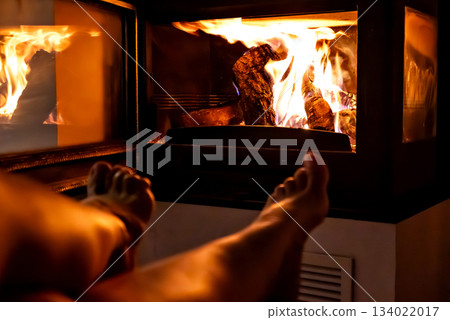 A pair of feet in front of the fireplace. A woman and man warm themselves by the fire. 134022017