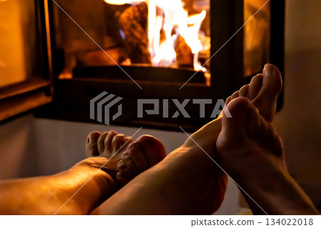 A pair of feet in front of the fireplace. A woman and man warm themselves by the fire. A pair of feet in front of the fireplace. A woman and man warm themselves by the fire. 134022018