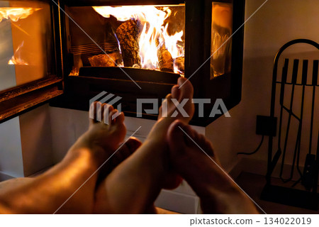 A pair of feet in front of the fireplace. A woman and man warm themselves by the fire. A pair of feet in front of the fireplace. A woman and man warm themselves by the fire. 134022019